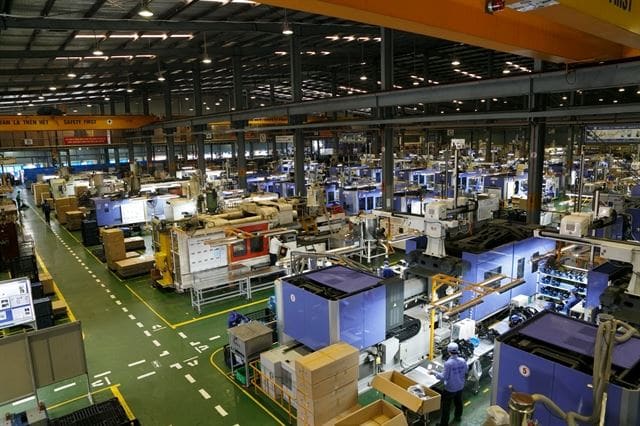 A wide view over a factory floor from above, with rows of machines and pallets of boxes between them